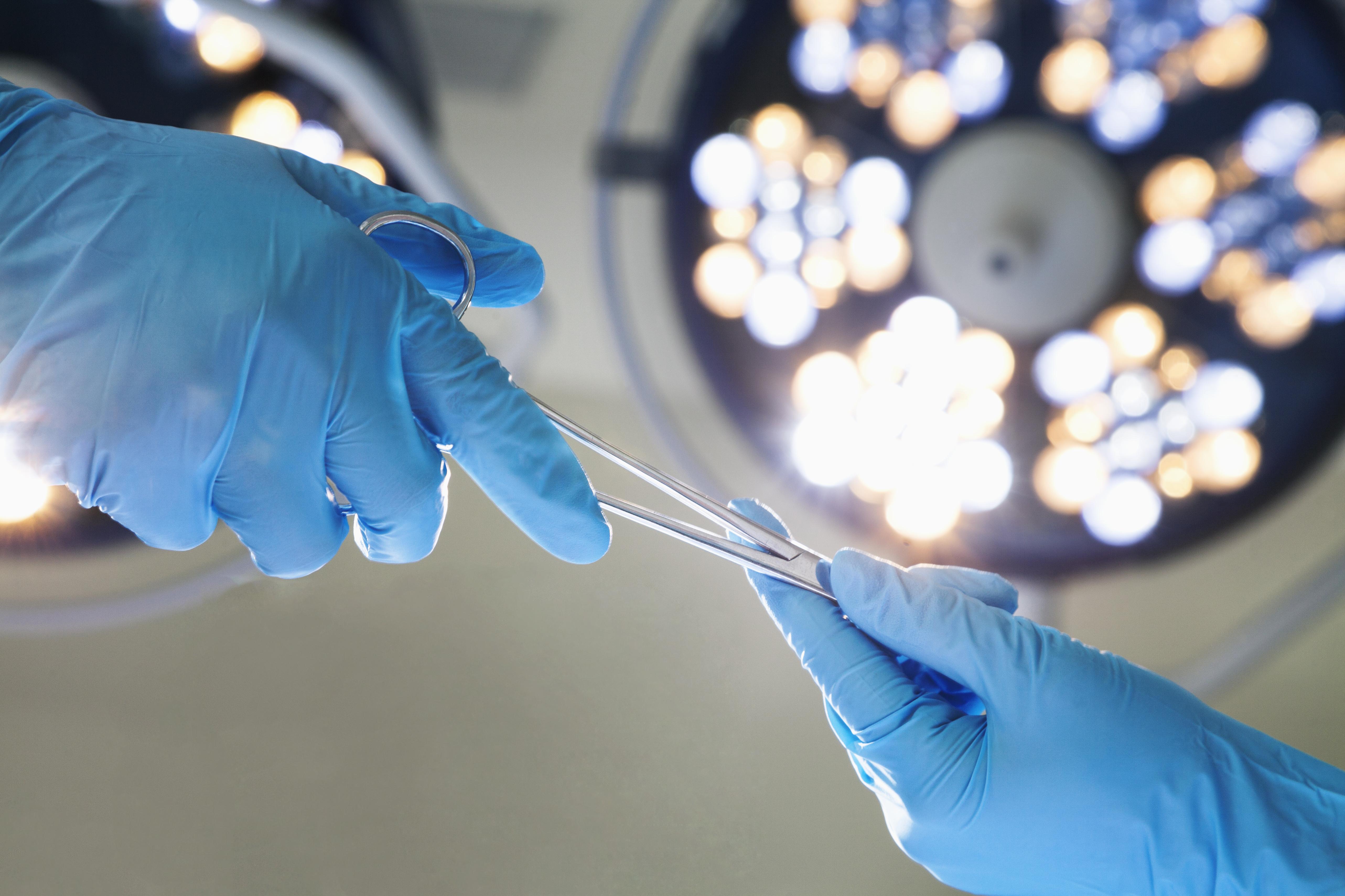 image of two gloved hands passing a surgical instrument under bright lights