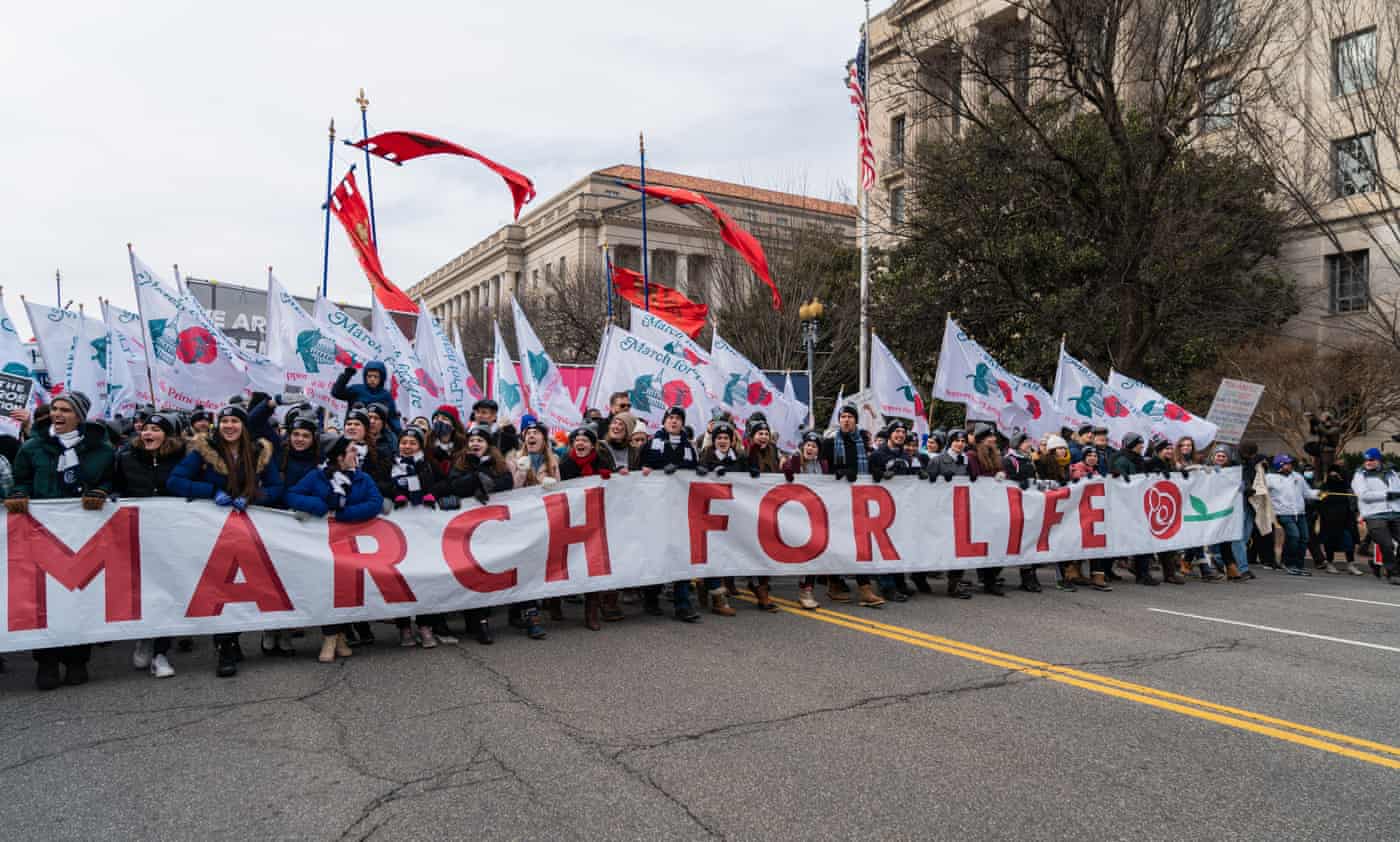 A crowd of women holding up white flags and a white banner that reads "MARCH FOR LIFE" in red