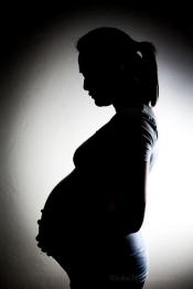 Silhouette of a pregnant body is shown, with their face pointed down and holding their stomach.