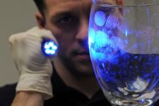 Investigator holds a forensic light to illuminate fingerprints on glass, revealing several visible fingerprints.