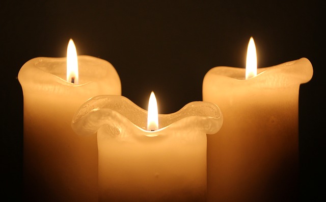 Three burning white candles, in a dark room. Candle wax drips on each.