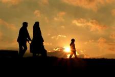 Silhouette of two adults and a child walking in front of a sunset