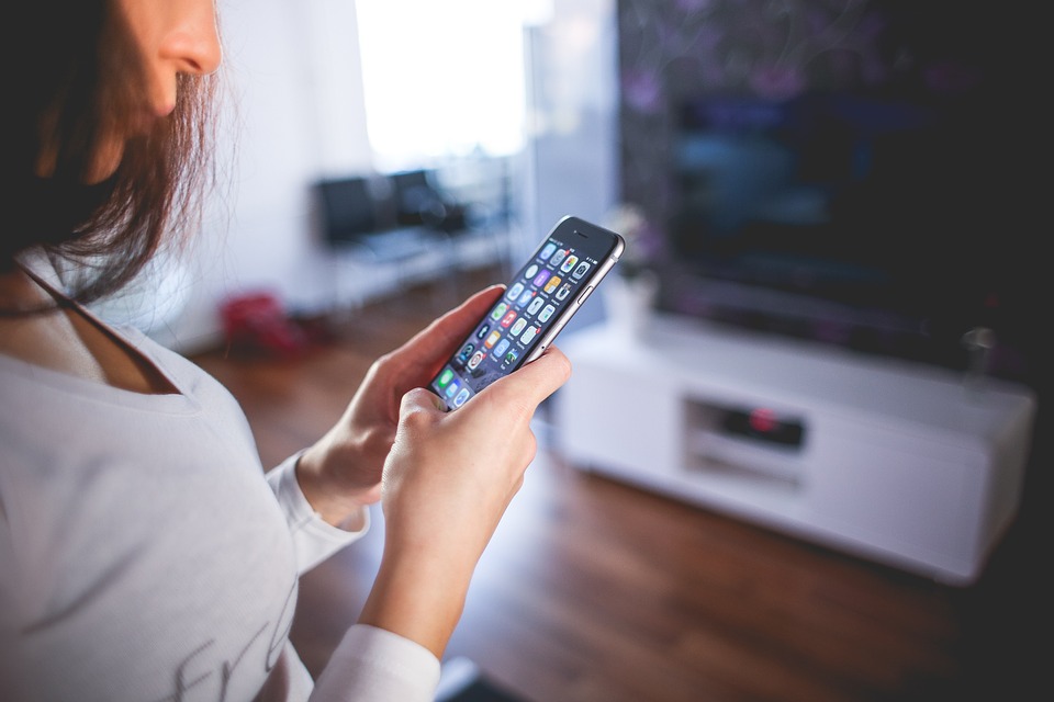 A woman is attentively drawn to the smart phone she holds in her hands.