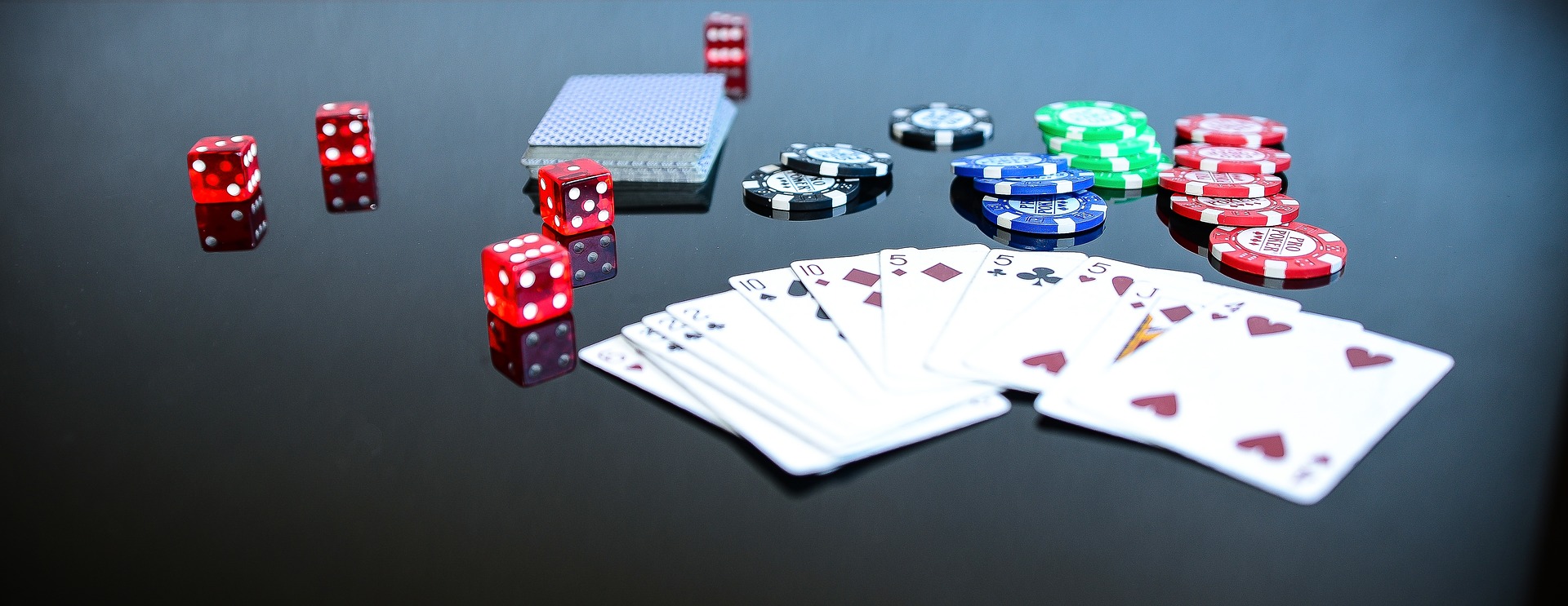 On a black table, many items are displayed: cards fanned out, rollingdice, and poker chips.