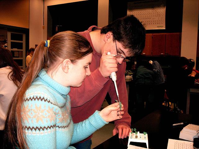 Two youths--a male and female-- concentrate in a lab procedure. The male holds a pipette. The female holds the sample. 