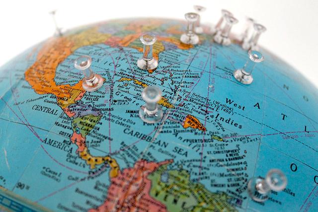 A close up photograph of a globe with clear push pins inserted in various countries.