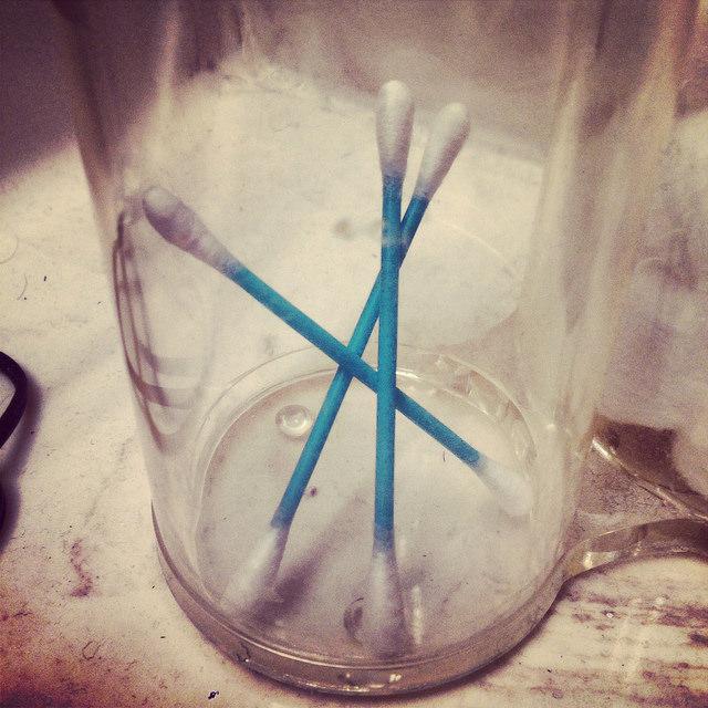 Three cotton swabs stand inside of a see-through glass container.