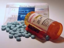 A bottle of prescribed morphine lays open. Light blue morphine tablets surround the bottle. Credit card appears out of focus in the background.