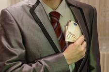 An individual's torso is pictured, wearing a gray business suit. The individual's hand is buried in their suit pocket, holding euros.