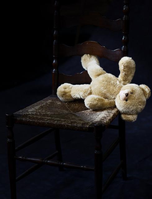 A teddy bear is turned on its side, on the floor of a darkened room.