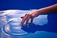 A hand touches the surface of water, creating a ripple effect from the center.