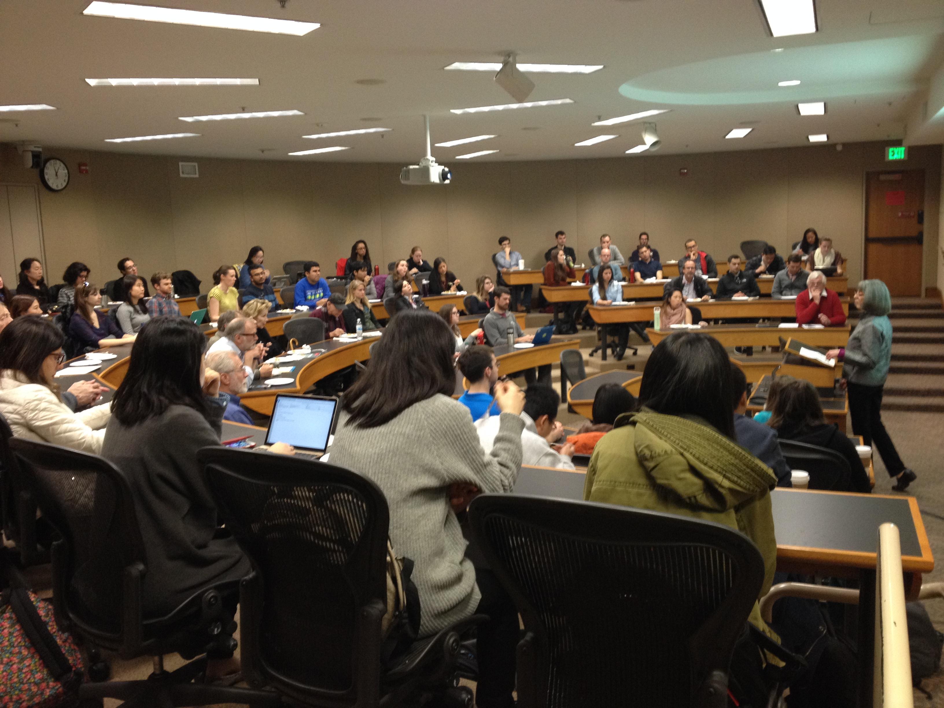 Marcy Darnovsky presents in front of a room full of people sitting in desks.