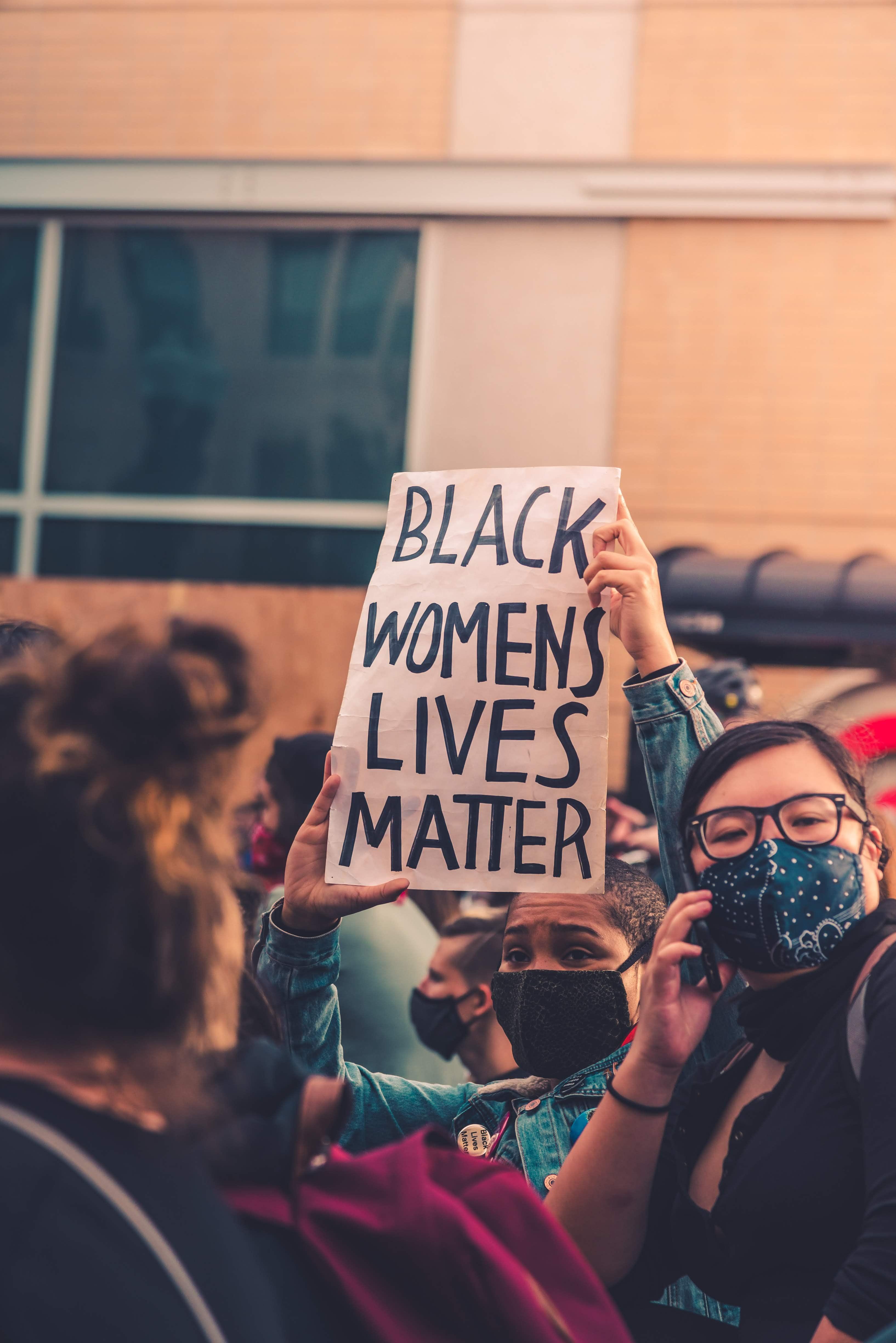 A person in a crowd at a black lives matter protest holding up a sign that says "black women's lives matter"