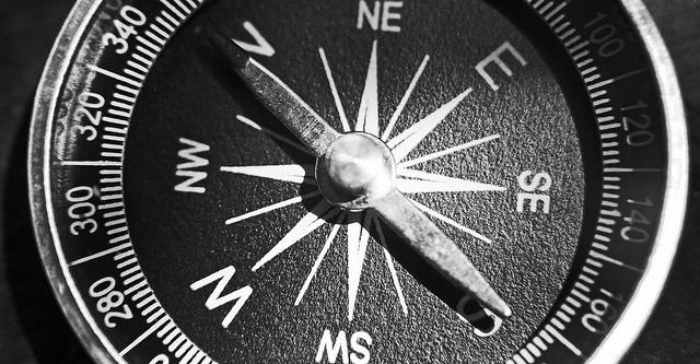 Gray-scale close-up of a compass. pointing north.