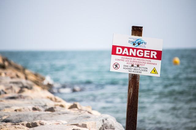 Near a beach cliff, there is a warning sign that reads in bold letters "Danger"