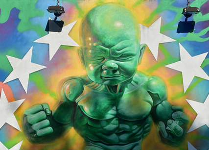 Street art depiction of a large, green baby with muscular chest and arms, surrounded by a semicircle of white stars against a multicolored background