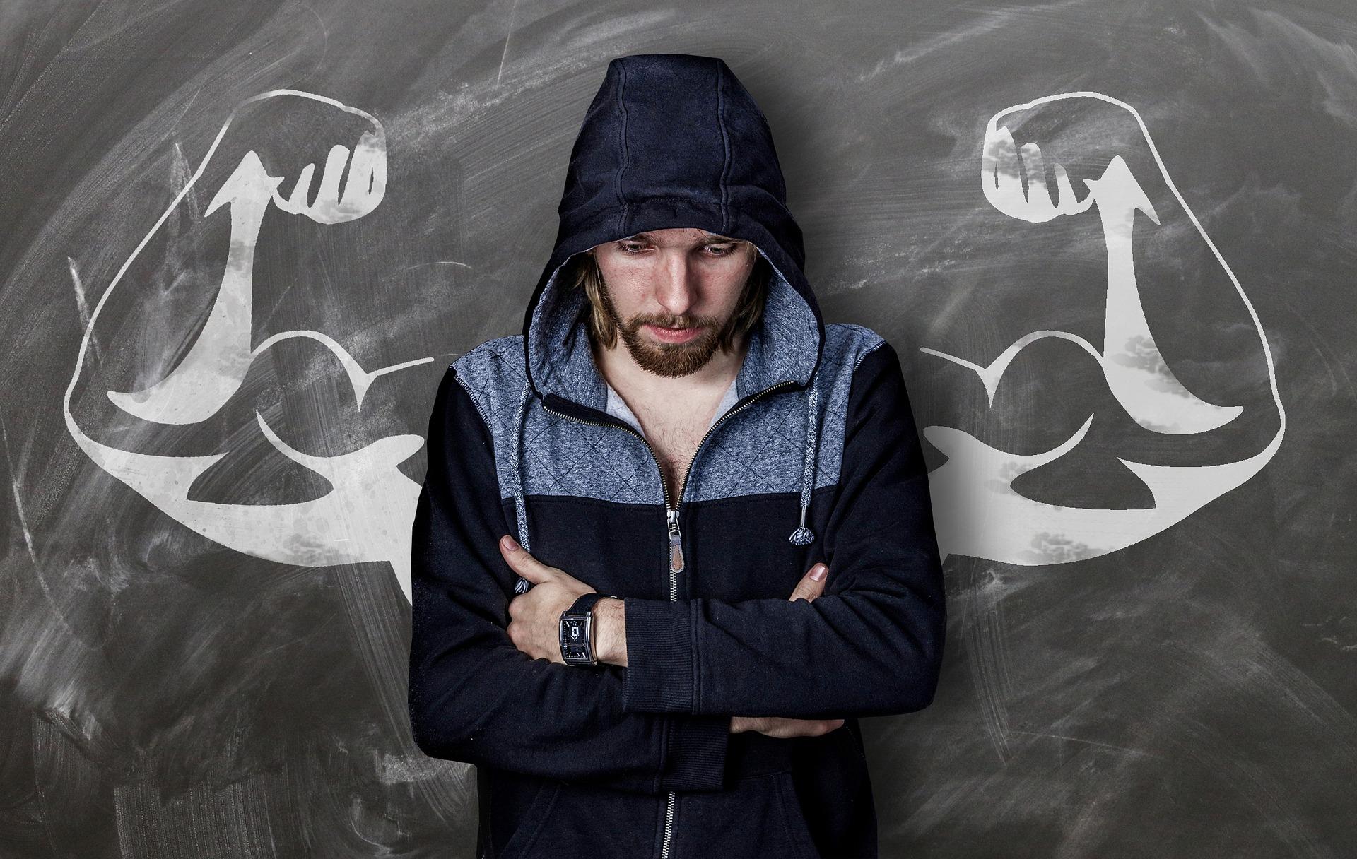 There is a chalk drawing of a strong man behind a smaller person wearing a hood and looking down.