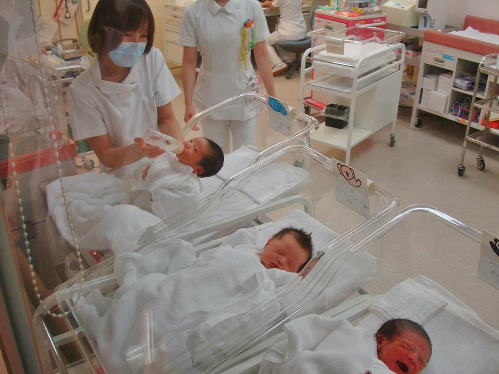 Three small babies in their hospital beds with a nurse taking care of one of them.