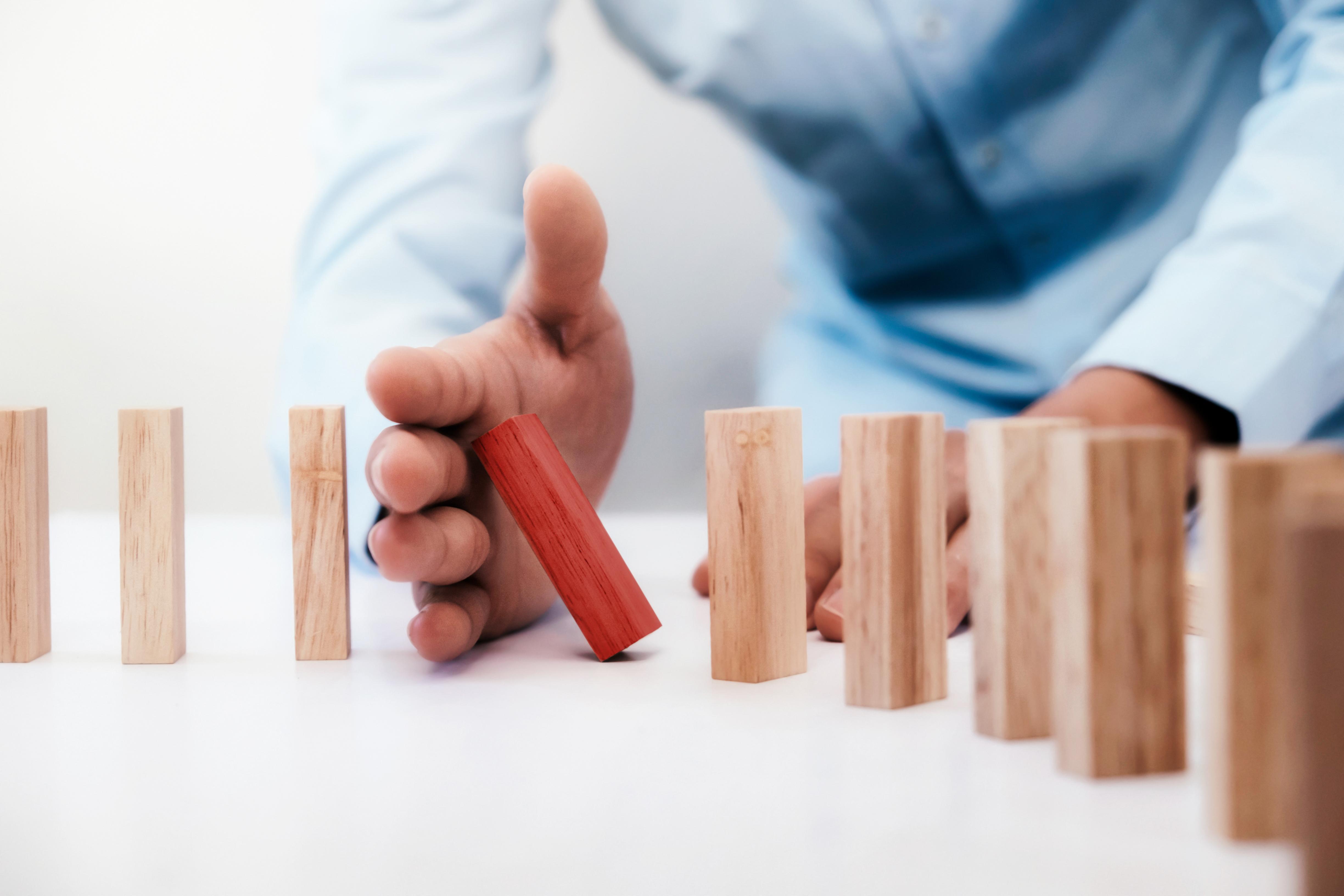 Hand stopping a red domino from toppling other dominos