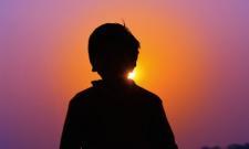 An outline of a child is silhouetted against a sunset background.