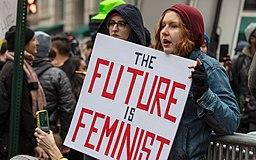 Two women are pictured holding a protest sign stating, "The future is feminist"