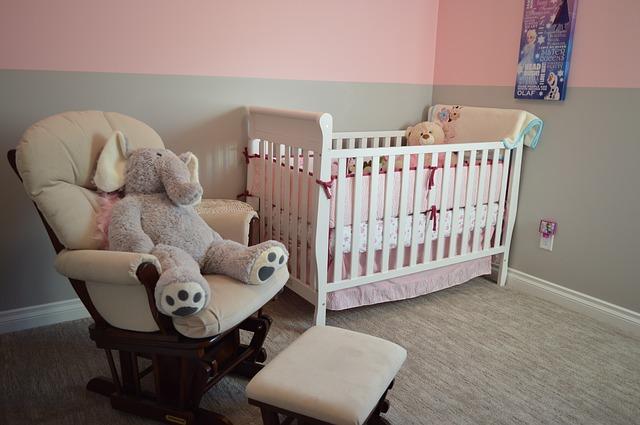 A cradle and a rocking chair occupy a baby room painted pink.
